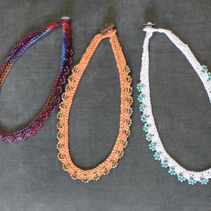 May include: Three beaded necklaces, one with a purple and red gradient, one with orange and brown beads, and one with white and teal beads.