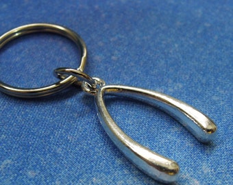 May include: A silver-toned metal wishbone charm attached to a circular split key ring. The wishbone has a smooth, polished, reflective surface and a Y-shaped structure. The key ring is a simple, thin, circular metal loop for holding keys.