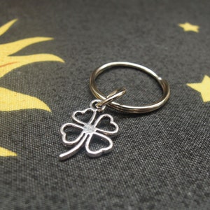 May include: A silver four-leaf clover charm attached to a silver key ring. The charm has a small clear rhinestone in the center.