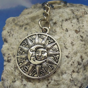 May include: Silver key chain with a circular charm featuring a sun and moon design. The charm has zodiac symbols around the edge.