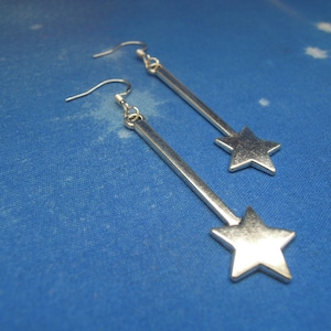 May include: A pair of silver star-shaped earrings with a long, thin, silver rod attached to each star.