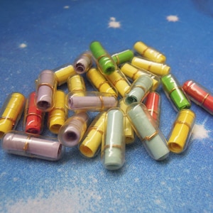 Puede incluir: Un montón de mensajes de papel coloridos y enrollados dentro de tubos de plástico transparentes con tapas doradas. Los tubos están dispuestos en un patrón aleatorio.