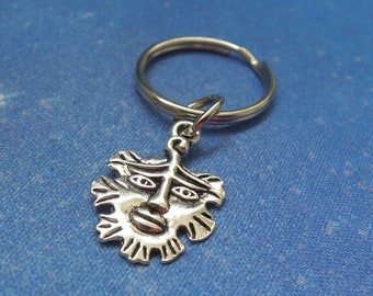 May include: Silver key chain with a detailed face charm. The face has a stylized design with a beard and two eyes.