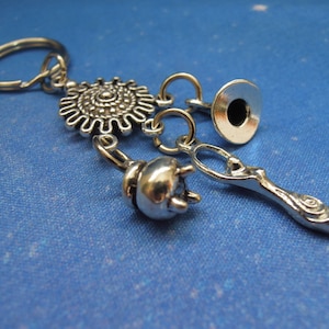 May include: Silver charm keychain with a circular charm, a bell charm, a small trumpet charm, and a charm shaped like a woman. The charms are attached to a silver key ring.