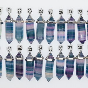 Puede incluir: Un conjunto de 16 colgantes de cristal de fluorita con una anilla de metal plateada. Los cristales son todos de diferentes tonos de azul, morado y verde. Los colgantes est&aacute;n numerados del 14 al 39.