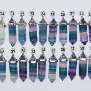 Puede incluir: Una colecci&oacute;n de 16 colgantes de cristal de fluorita con una anilla de metal plateada. Los cristales son todos de diferentes tonos de azul, morado y verde. Los colgantes est&aacute;n numerados del 14 al 39.