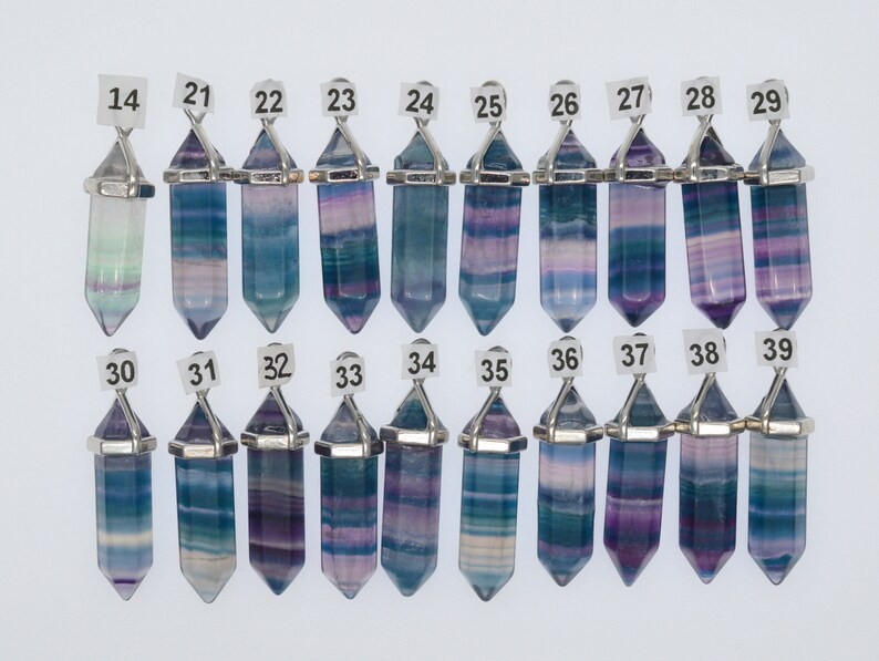 Puede incluir: Una colecci&oacute;n de 16 colgantes de cristal de fluorita con una anilla de metal plateada. Los cristales son todos de diferentes tonos de azul, morado y verde. Los colgantes est&aacute;n numerados del 14 al 39.