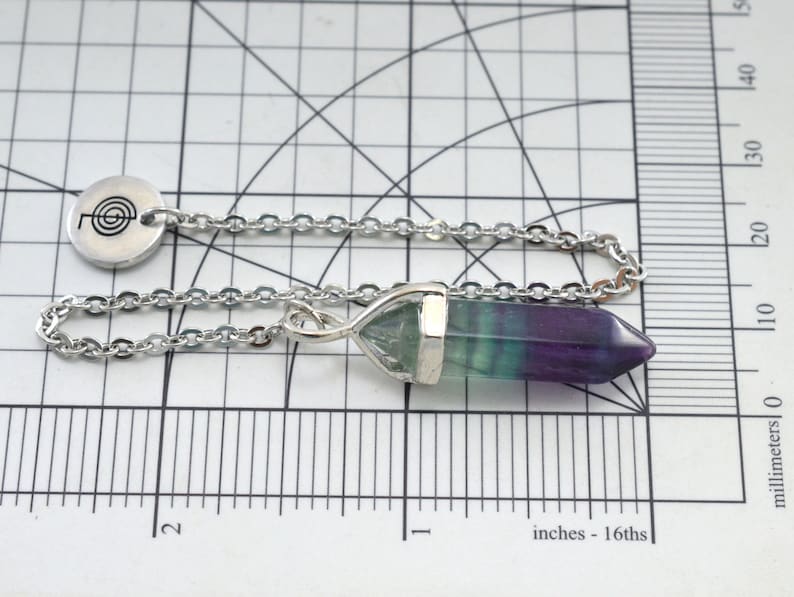 Puede incluir: Una cadena de plata con un colgante de plata que presenta una punta de cristal de fluorita verde, azul y p&uacute;rpura. El colgante tambi&eacute;n tiene un dije de plata con un s&iacute;mbolo en espiral.