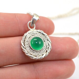 May include: A silver pendant necklace featuring a round, bright green gemstone set within a woven silver frame. The pendant hangs from a delicate silver chain. The design is simple yet elegant, suitable for everyday wear.