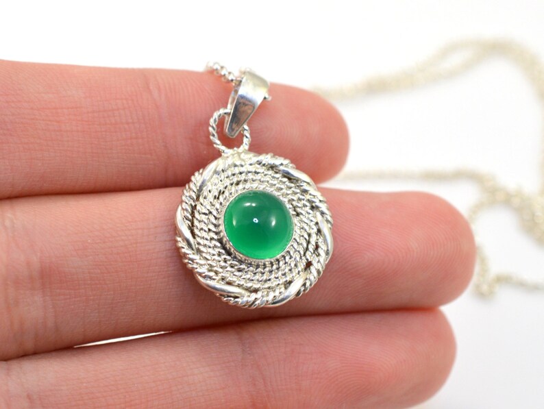 May include: A silver pendant necklace featuring a round, bright green gemstone set within a woven silver frame. The pendant hangs from a delicate silver chain. The design is simple yet elegant, suitable for everyday wear.