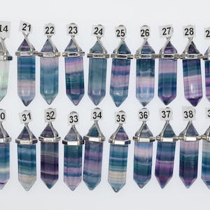 Puede incluir: Una colecci&oacute;n de 16 colgantes de cristal de fluorita con engastes de metal plateado. Los cristales son todos de diferentes tonos de azul, morado y verde, algunos con vetas blancas. Los colgantes est&aacute;n numerados del 14 al 39.