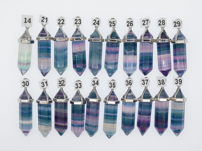 Puede incluir: Una colecci&oacute;n de 16 colgantes de cristal de fluorita con engastes de metal plateado. Los cristales son todos de diferentes tonos de azul, morado y verde, algunos con vetas blancas. Los colgantes est&aacute;n numerados del 14 al 39.