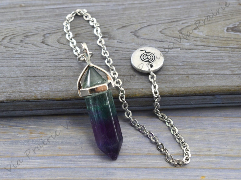 Puede incluir: Un p&eacute;ndulo de cristal de fluorita verde, morado y azul con una cadena de plata y un dije de plata con un s&iacute;mbolo.
