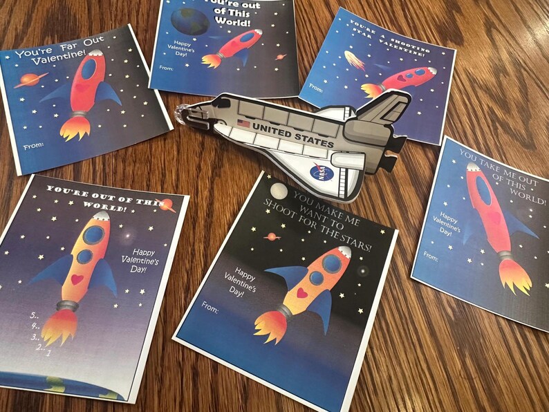 Puede incluir: Un conjunto de diez tarjetas de San Valent&iacute;n con tem&aacute;tica espacial. Las tarjetas tienen un fondo azul con estrellas y planetas. Cada tarjeta presenta una nave espacial y un mensaje diferente para el D&iacute;a de San Valent&iacute;n. Los mensajes incluyen "You're Far Out Valentine!" y "You Make Me Want To Shoot For The Stars!"