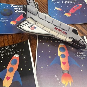 Puede incluir: Cuatro tarjetas de San Valent&iacute;n con tem&aacute;tica espacial. Las tarjetas tienen cohetes, estrellas y el texto "You're a shooting star Valentine!" y "Make me want to go to the stars!"