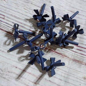 May include: A collection of small, dark blue decorative objects, each with a bow-like design and a cylindrical component. The objects are scattered on a light-colored, patterned surface, casting shadows.
