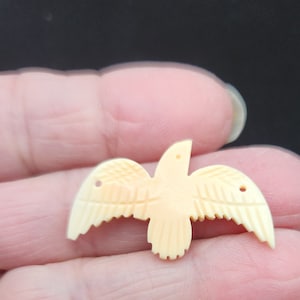 Può includere: Un ciondolo a forma di uccello in avorio intagliato con dettagli intricati. L'uccello è in posizione di volo con le ali spiegate. Il ciondolo è di colore crema chiaro.