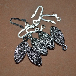 May include: Silver metal clasps with decorative, textured, oval-shaped pieces. The clasps have a hook and loop design.