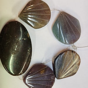 Pode incluir: Uma sequência de cinco contas de pedras preciosas, cada uma com um formato e cor únicos. As contas são uma mistura de marrom, verde e roxo, com um padrão estriado. As contas são enfiadas em um fio fino.