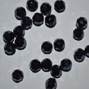 以下が含まれることがあります： 黒いファセットガラスビーズのコレクション。ビーズは丸く、光沢のある仕上げになっています。