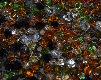 May include: A close-up of a variety of small, faceted glass beads in shades of green, brown, and clear. The beads are scattered on a dark surface.