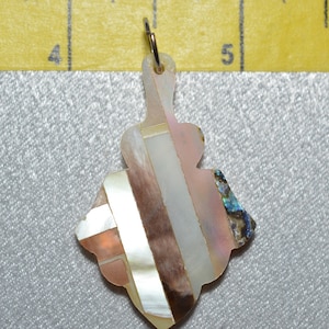 Può includere: Un ciondolo in madreperla iridescente con un design geometrico. Il ciondolo è attaccato a un anello d'argento.