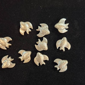 May include: A collection of eleven silver-colored fish charms. The charms are all the same size and shape, and they are arranged in a random pattern on a black background.
