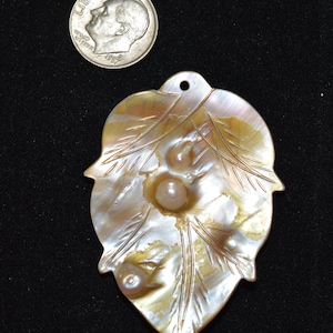 May include: A carved mother-of-pearl pendant with three iridescent pearls set in the centre. The pendant is shaped like a leaf with a hole at the top for hanging.