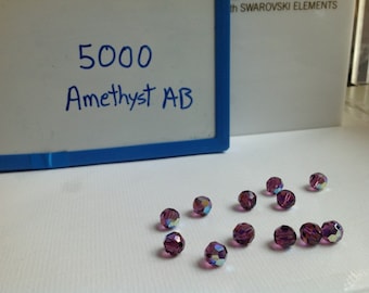 May include: A close-up of 5000 amethyst AB beads. The beads are round and have a purple iridescent finish.