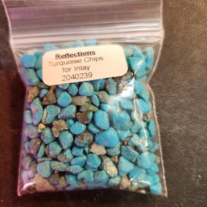 Puede incluir: Una bolsa de plástico transparente llena de virutas de turquesa para incrustaciones. La etiqueta dice "Reflections Turquoise Chips for Inlay 2040239". Las virutas son de un color azul verdoso vibrante, con algunas inclusiones marrones y grises.