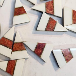 May include: A collection of triangular ceramic tiles with a white background and a red and gold stripe design.