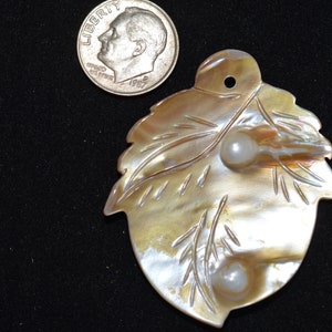 May include: A shell pendant featuring a leaf design and two pearls. The shell is a light brown colour with a pearlescent sheen. The pearls are white and round.