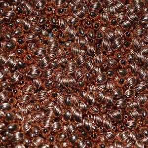 Puede incluir: Una gran cantidad de pequeñas cuentas ovaladas de color cobre. Las cuentas tienen una superficie texturizada y nervada.