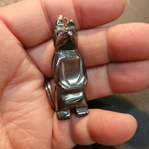 May include: A black obsidian wolf pendant with a silver loop for a chain. The wolf is carved in a standing position with its head tilted up.
