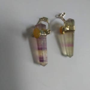 May include: A pair of earrings featuring a purple and white fluorite crystal with a yellow gemstone accent. The crystals are attached to silver-toned metal.
