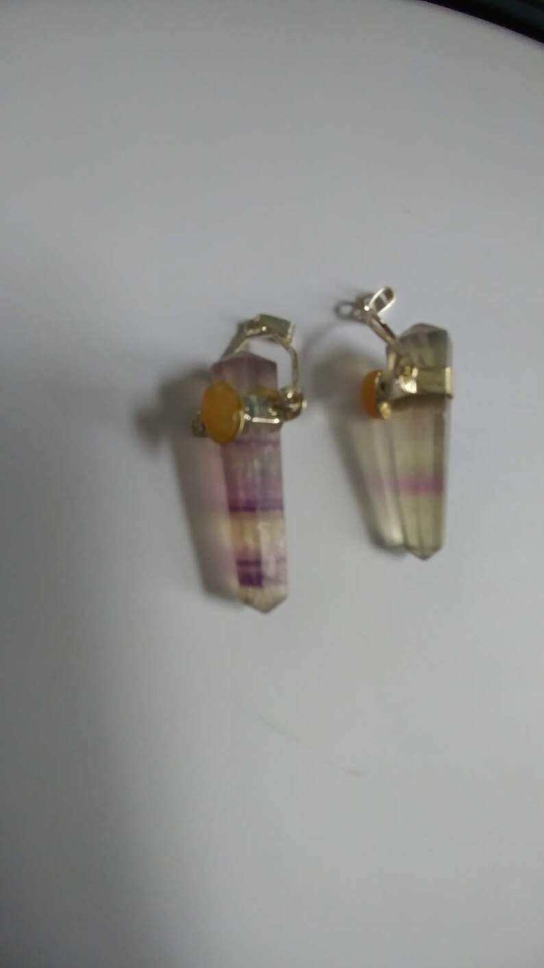May include: A pair of earrings featuring a purple and white fluorite crystal with a yellow gemstone accent. The crystals are attached to silver-toned metal.