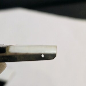 May include: Close-up of a black and white striped metal object with a small hole in the center.