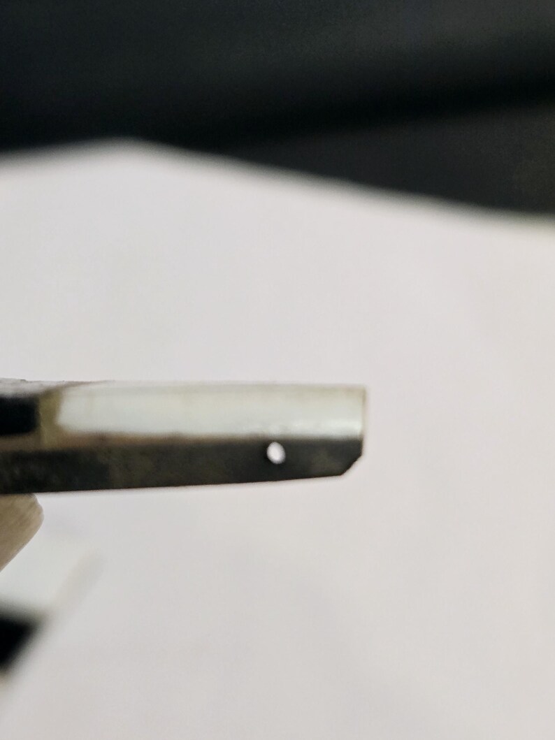 May include: Close-up of a black and white striped metal object with a small hole in the center.
