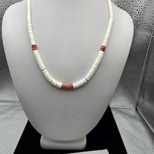 以下が含まれることがあります： 白ビーズネックレス、コーラルカラーのアクセント付き。白いマネキンに飾られています。ビーズは小さくて丸く、ネックレス全体にコーラルカラーのビーズが散りばめられています。