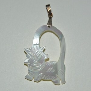May include: A white mother of pearl pendant featuring a carved cat design. The cat is sitting with its tail curled around its body. The pendant has a silver loop for attaching to a chain.