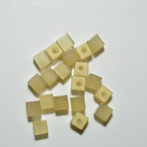 May include: A group of small, square, translucent, light yellow beads with a hole in the center of each bead.