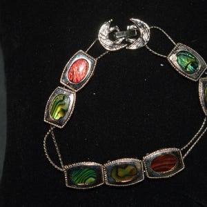 May include: A silver bracelet with six oval-shaped green, red, and iridescent abalone shell inlays.