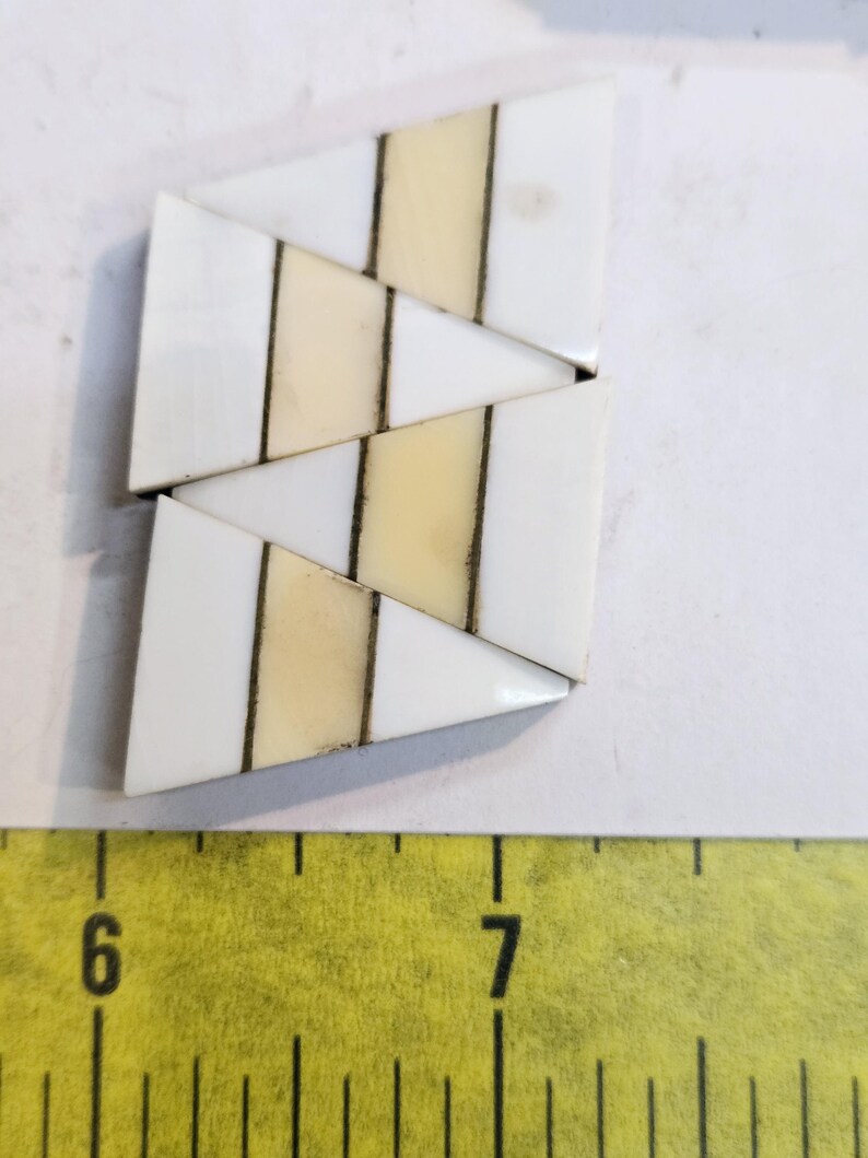 May include: A set of three white and cream triangular tiles with black lines. The tiles are arranged in a staggered pattern.