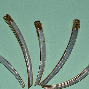 May include: Five ivory-colored, curved, decorative objects with gold accents. The objects are arranged in a fan shape.