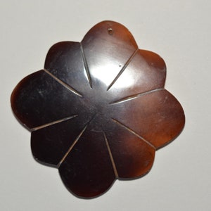 May include: A dark brown, flower-shaped pendant with eight petals. The pendant has a glossy finish and a small hole at the top for hanging. The design features subtle lines radiating from the center, adding detail to the piece.