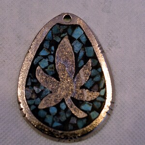 May include: A silver pendant shaped like a teardrop with a turquoise inlay and a silver leaf design.