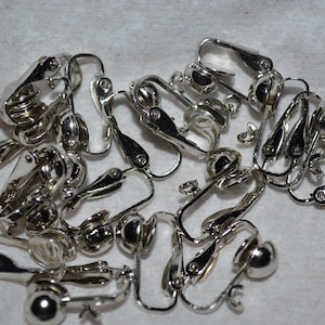 May include: A close-up of a pile of silver-toned earring clips. The clips are made of metal and have a round ball at the end. They are designed to be used with earrings that do not have a post.
