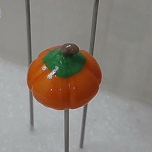 May include: Four decorative pumpkin picks. Each pumpkin is orange with a green stem and sits atop a thin, silver metal stick. These fall-themed decorations are perfect for adding a festive touch to floral arrangements or seasonal crafts.