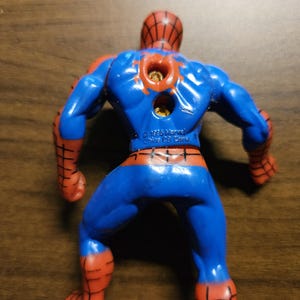 May include: A blue and red Spider-Man action figure, viewed from the back. The figure has a red spiderweb pattern on the head and arms, with blue on the body and legs. The figure is marked with "&copy; 1995 Marvel China CB China".