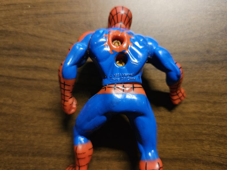 May include: A blue and red Spider-Man action figure, viewed from the back. The figure has a red spiderweb pattern on the head and arms, with blue on the body and legs. The figure is marked with "&copy; 1995 Marvel China CB China".